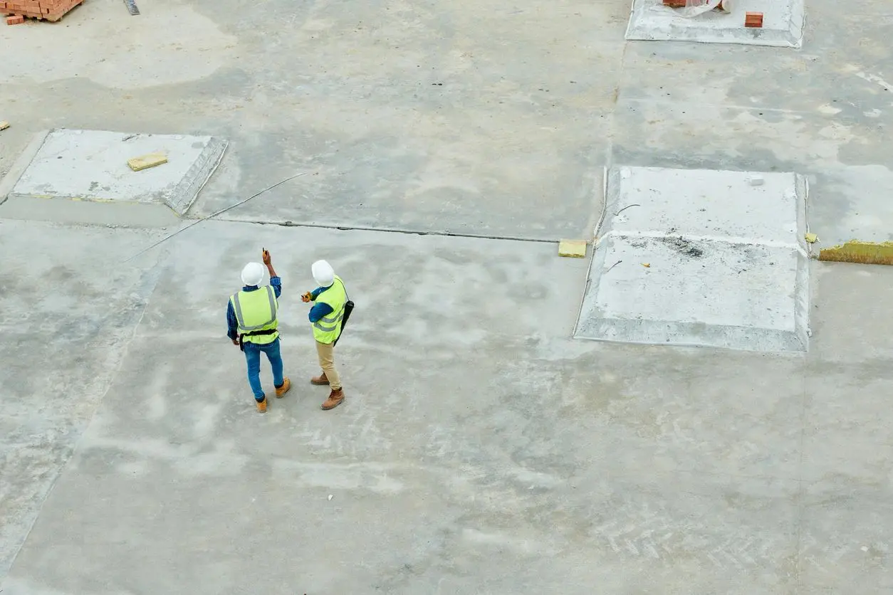 Two construction workers standing on a concrete slab.